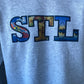 St. Louis STL Sweatshirt of St. Louis, Missouri containing images of the St. Louis flag, toasted raviolis, amd the Gateway Arch. 